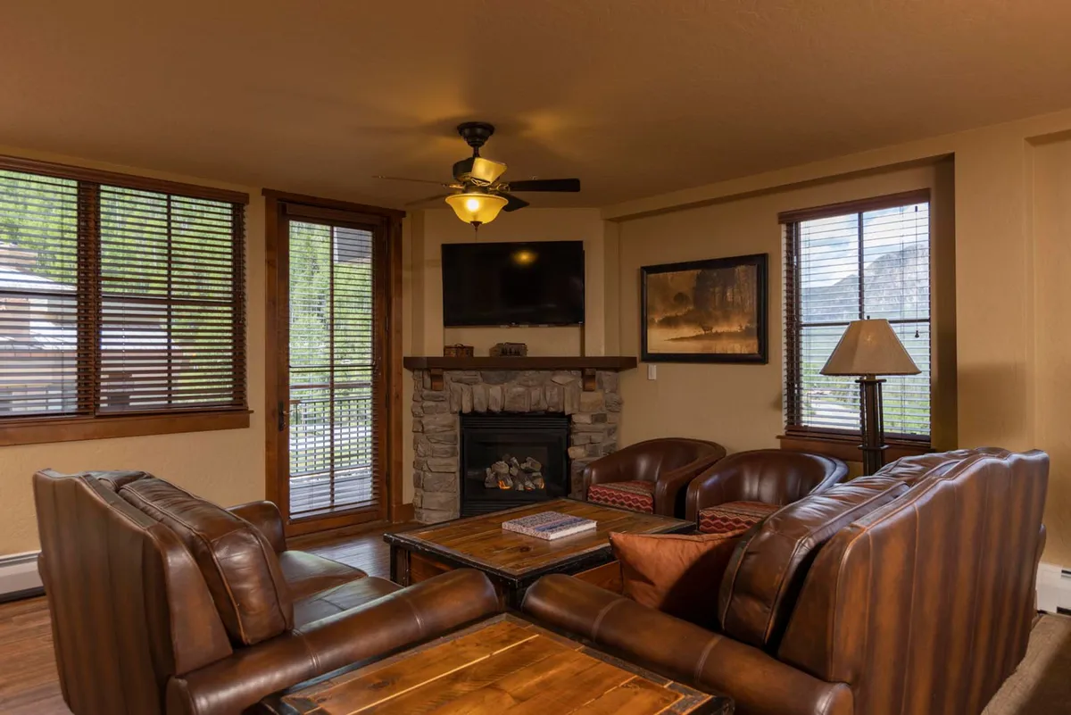 A cozy lounge area featuring a stone fireplace, leather armchairs, a wooden coffee table, and a wall-mounted TV. The atmosphere is warm and welcoming, ideal for socializing, friendly competition, or quiet moments after a day of adventure.