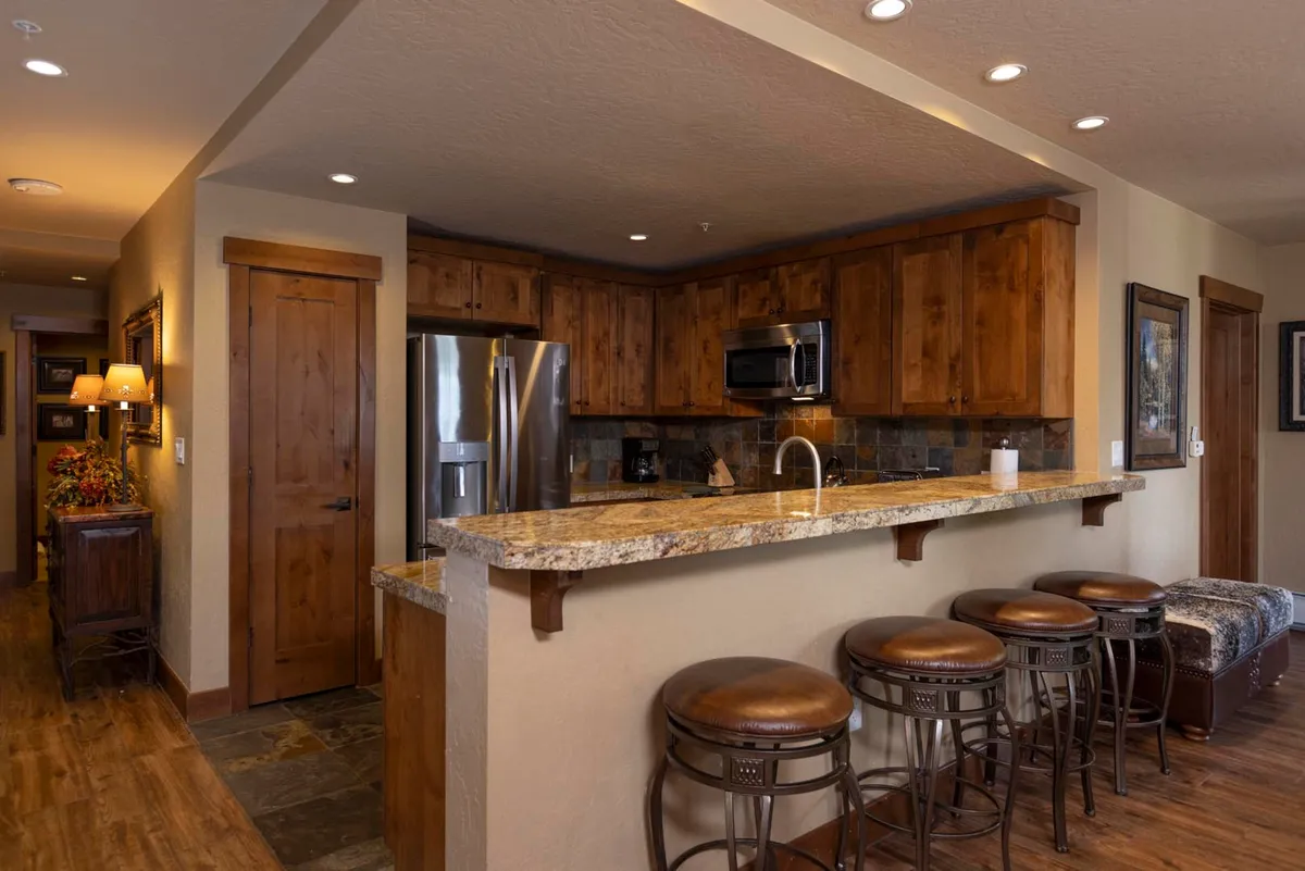 An inviting kitchen scene featuring a granite countertop, wooden cabinets, bar stools, and modern appliances. The space is set up for cooking, entertaining, and casual dining, perfect for hosting family dinners or group brunches.