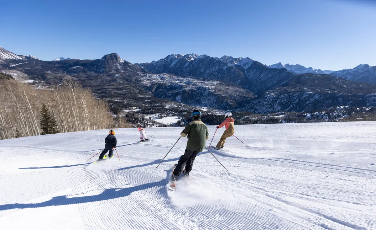 The image captures skiers in action on snow-covered slopes, framed by a breathtaking mountain backdrop. The energy and excitement of winter sports are palpable, with crisp white snow and clear skies highlighting the thrill of ski-in/ski-out living.
