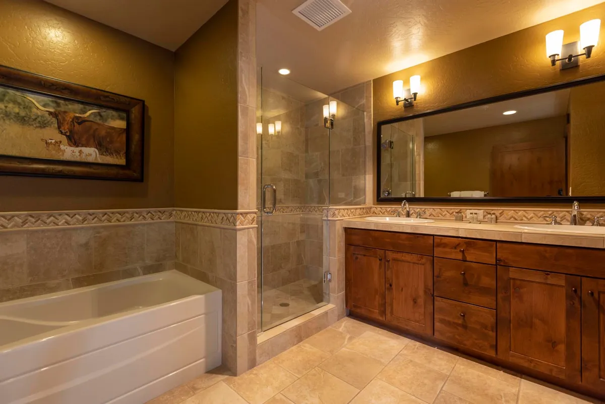A luxurious bathroom featuring a bathtub, glass shower enclosure, double sink vanity with a large mirror, and tasteful framed artwork. The space is modern, spacious, and exudes a sense of calm ideal for relaxation and rejuvenation.