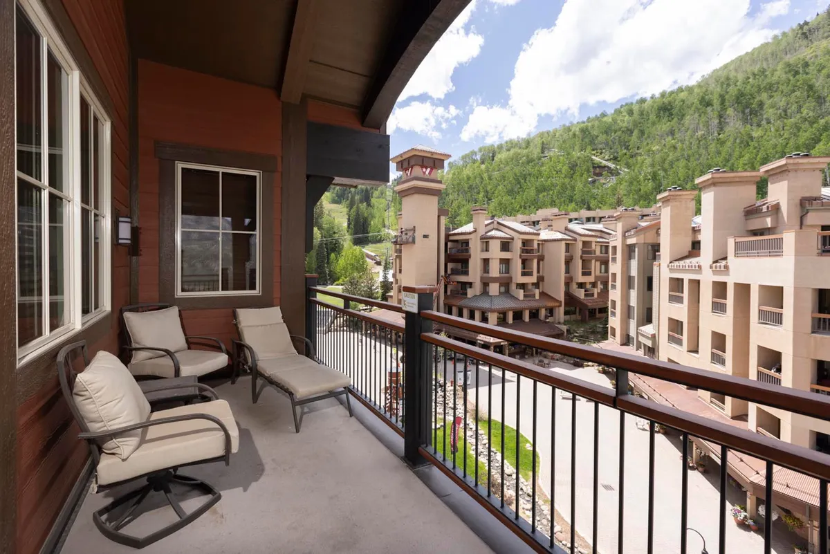 A private balcony with comfortable seating that overlooks breathtaking mountain scenery and nearby resort architecture. The peaceful setting is perfect for relaxing outdoors, sipping coffee, or socializing while enjoying the view.